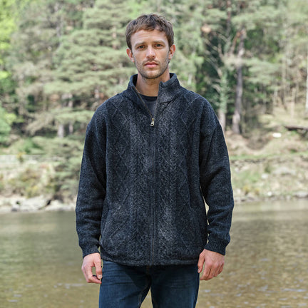 Man wearing a dark jacket standing by a body of water with trees in the background