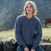 Woman wearing a blue knitted sweater sitting outdoors with mountains in the background