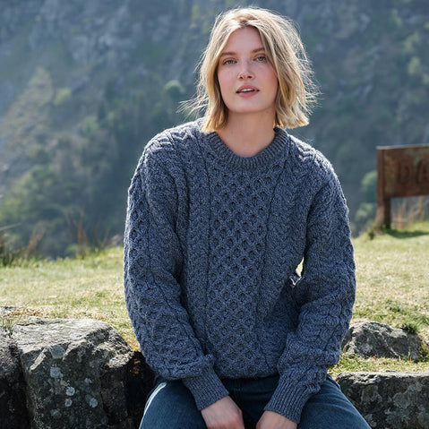 Woman wearing a blue knitted sweater sitting outdoors with mountains in the background