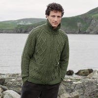Image featuring the Men's Hand Knit Aran Zipper Cardigan in green, crafted with authentic Irish Aran cable knit patterns, a full-zip fastening, and a high ribbed collar, showcasing traditional Irish craftsmanship against a scenic coastal landscape.
