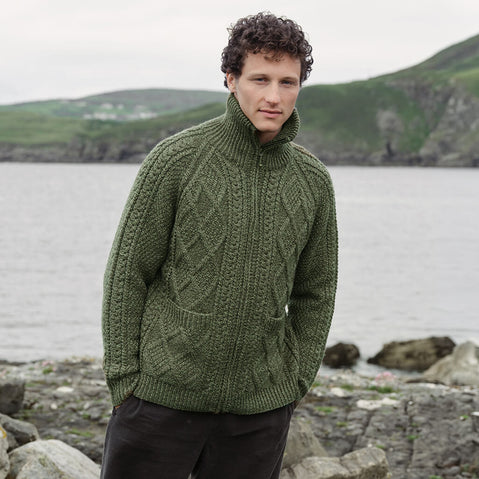 Image featuring the Men's Hand Knit Aran Zipper Cardigan in green, crafted with authentic Irish Aran cable knit patterns, a full-zip fastening, and a high ribbed collar, showcasing traditional Irish craftsmanship against a scenic coastal landscape.