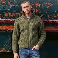 Man wearing a green Men's Hand Knit Aran Zipper Cardigan against a colorful, textured wall.