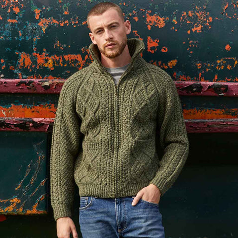 Man wearing a green Men's Hand Knit Aran Zipper Cardigan against a colorful, textured wall.