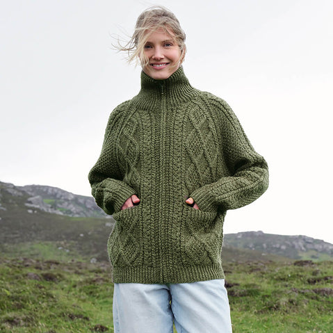 Image featuring the Women's Hand Knit Aran Zipper Cardigan in green, crafted with authentic Irish Aran cable knit patterns, a full-zip fastening, and a high ribbed collar, showcasing traditional Irish craftsmanship in a scenic countryside setting.