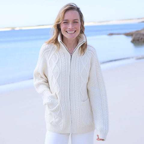 Woman wearing a cream Women's Hand Knit Aran Zipper Cardigan on a beach