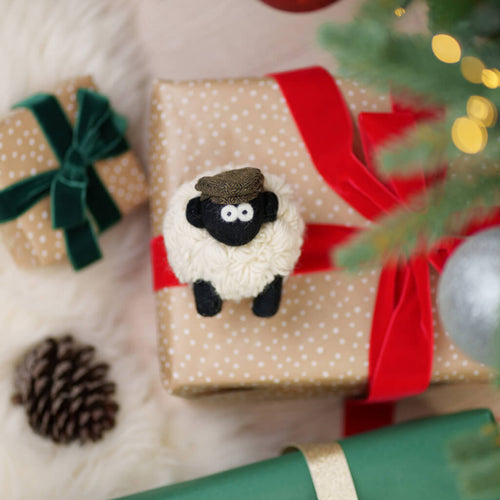 Gift box with a sheep ornament and red ribbon, surrounded by Christmas decorations.