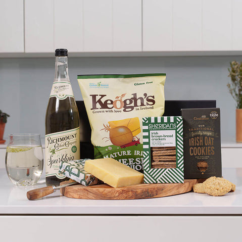 Irish picnic gift basket with cheese, crackers, oat cookies and sparkling drink arranged on serving board