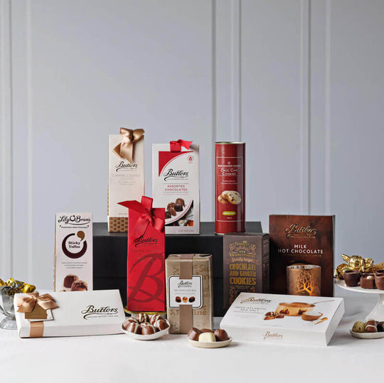 Indulgent Irish Chocolate Gift Collection. A selection of assorted chocolates and Irish treats is displayed on a light backdrop. Various elegantly packaged boxes, including chocolate truffles and cookies, are arranged prominently. The chocolates feature luxurious branding and decorative ribbons, showcasing a variety of flavors and styles.