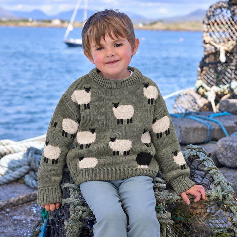 Child wearing a green premium soft wool sweater with black and white sheep design by the waterfront