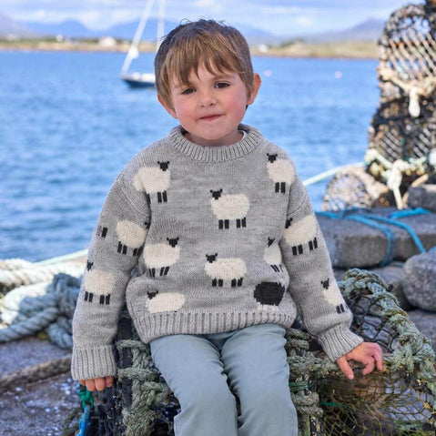 Child wearing a grey premium soft wool sweater with black and white sheep design by the waterfront