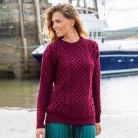 Woman wearing a claret Women's Crew Neck Irish Wool Classic Sweater by a body of water with boats in the background