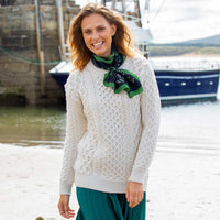 Woman wearing a cream Women's Crew Neck Irish Wool Classic Sweater and green scarf by a body of water with a boat in the background
