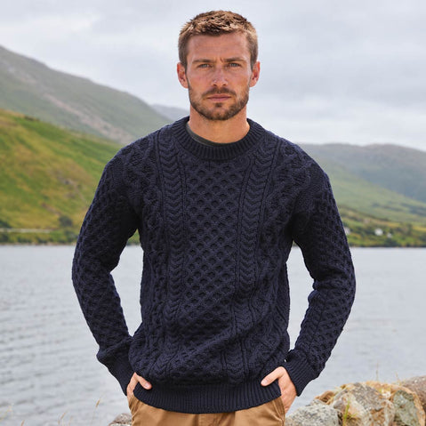 Image featuring the Men's Crew Neck Irish Wool Classic Sweater in navy, crafted from premium Irish wool with authentic cable knit patterns and a timeless crew neck silhouette, showcasing traditional Irish craftsmanship against a scenic lakeside mountain landscape.