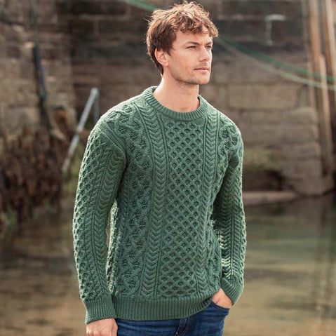 Man wearing a green Men's Crew Neck Irish Wool Classic Sweater standing outdoors with a rustic background