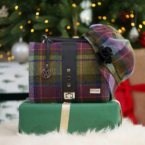 Mucros purple and green tartan plaid handbag with matching Ladies newsboy cap displayed on wrapped gift box with festive Christmas lights and ornaments in background