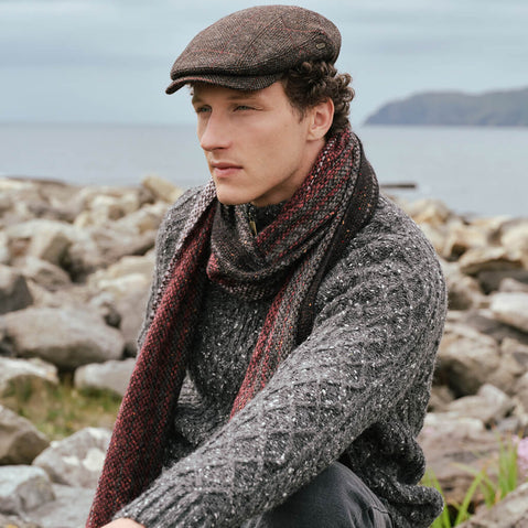 Peaky Blinders Wool Cap in Brown Red, featuring a classic heritage tweed design and timeless Irish craftsmanship, styled alongside traditional Irish knitwear and a luxury alpaca scarf against the rugged Irish coastline.