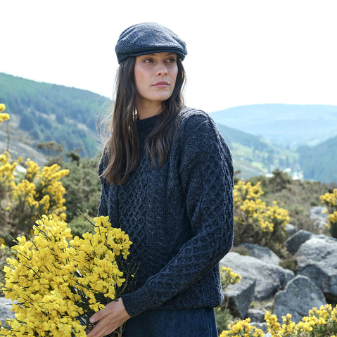 Woman in a blue knitted sweater and cap holding yellow flowers with a mountainous background