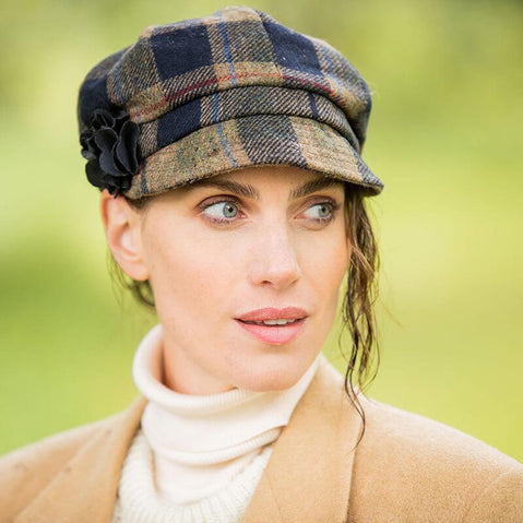 A woman wearing a beige Irish wool newsboy cap with a leather flower motif on the side.