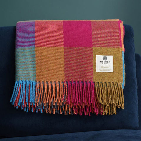 Irish home décor- A multicolored lambswool check throw with fringes displayed on a dark sofa.