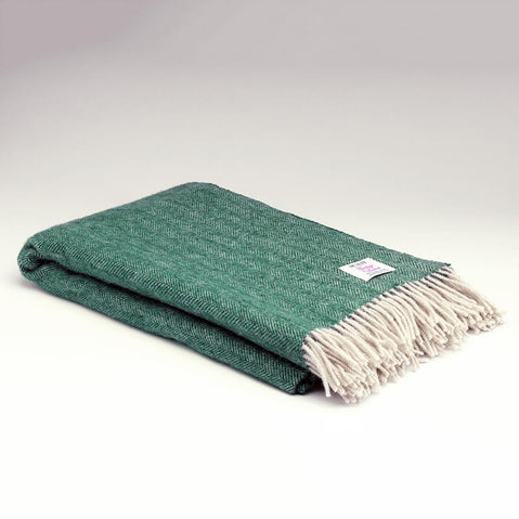 Folded Mc Nutt spruce‑green herringbone blanket with cream fringe detailing displayed on a light background.