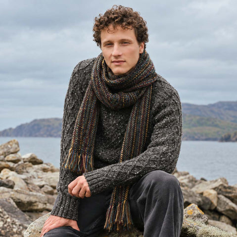 Image featuring the Men's Alpaca Islander Scarf in brown, crafted from a soft alpaca blend with a rich multicoloured flecked design and classic fringed finish, showcasing timeless Irish-inspired style against a rugged coastal landscape.