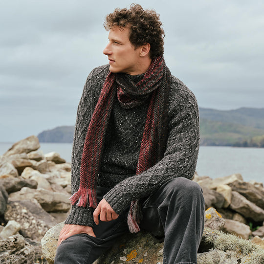 Men's Alpaca Islander Scarf in Cranberry, crafted from luxuriously soft alpaca wool with a rich textured weave, styled with traditional Irish knitwear against the rugged Irish coastline for a timeless heritage look.
