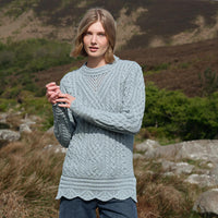 Woman wearing a mermaid blue-colored Women's Signature Aran Tunic Sweater from The Irish Store, featuring traditional Aran stitching and a cozy, elegant fit