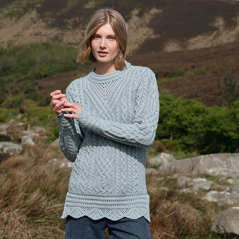 Woman wearing a mermaid blue-colored Women's Signature Aran Tunic Sweater from The Irish Store, featuring traditional Aran stitching and a cozy, elegant fit
