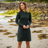A woman standing on a beach wearing a long sleeve cable knit aran dress in green color.