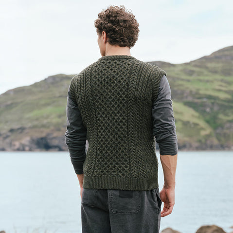 Back view of the Men's Traditional Fisherman Zipper Vest in green, crafted with authentic Irish fisherman cable knit patterns and a timeless sleeveless silhouette, showcasing traditional Irish craftsmanship against a scenic coastal landscape inspired by Ireland's rugged countryside.