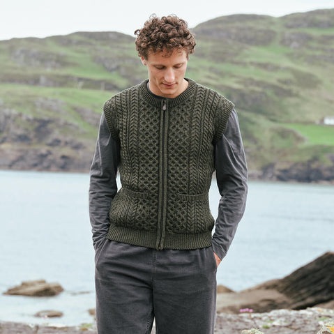 Image featuring the Men's Traditional Fisherman Zipper Vest in green, crafted with authentic Irish fisherman cable knit patterns, a practical full-zip fastening, and classic front patch pockets, showcasing timeless Irish craftsmanship against a scenic coastal landscape.