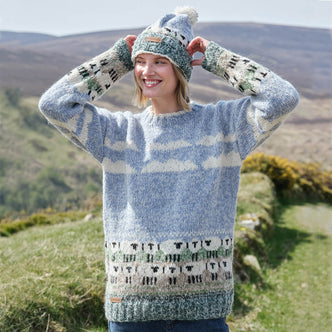 Woman wearing a patterned sheep sweater and matching hat in a scenic outdoor setting