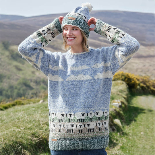 Woman wearing a patterned sheep sweater and matching hat in a scenic outdoor setting