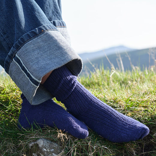 Person wearing blue wool socks with jeans in a grassy outdoor setting