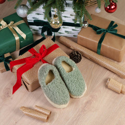 Merino Wool Slippers in mint green with fuzzy texture and cream soles displayed among wrapped Christmas gifts, pine garland, ornaments, and gold wrapping paper