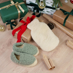 Merino Wool Slippers in mint green and cream Merino Hot Water Bottle Cover arranged with wrapped Christmas presents, pine garland, and festive decorations