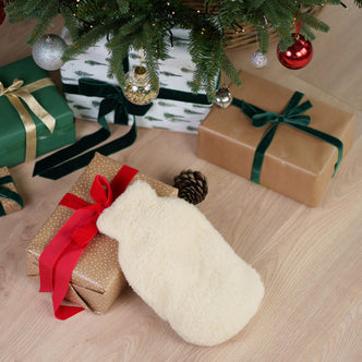 Merino Hot Water Bottle Cover - White knit Christmas stocking with wrapped gifts in green and gold paper with ribbons under a decorated Christmas tree