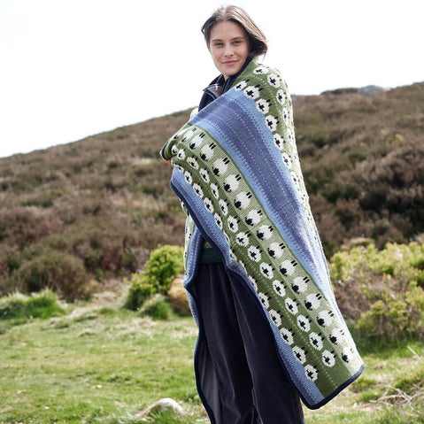 Woman standing outdoors wearing a green and blue sheep pattern blanket