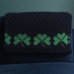 Navy Green Shamrock Merino Wool blanket hanged on a blue couch