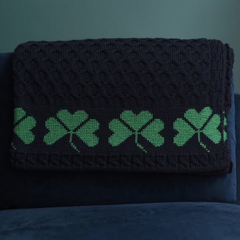 Navy Green Shamrock Merino Wool blanket hanged on a blue couch