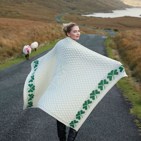 Person walking on a country road wrapped in a cream Shamrock Merino Wool Blanket featuring green shamrock patterns along the edges.