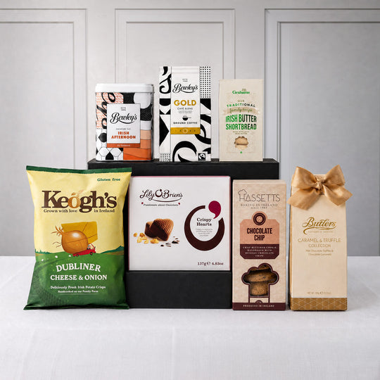 A luxury Irish food gift basket arranged in a black presentation box, featuring authentic Irish treats including Bewley's Irish Afternoon Tea, Bewley's Gold Blend Coffee, Keogh's Dubliner Cheese & Onion Crisps, Graham's Irish Butter Shortbread, Lily O'Brien's Crispy Hearts chocolates, Hassett's Chocolate Chip biscuits, and Butlers Caramel & Truffle chocolates. The elegant gift hamper is displayed against a neutral background, making it an ideal Irish gift for family, friends, and special occasions in the US