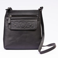 A black leather shoulder bag with embossed Celtic knotwork on the front and a visible zipper pocket. It has a single shoulder strap and a main compartment.