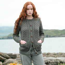 Image featuring The Banna Aran Cardigan in Tundra, crafted with authentic Irish Aran cable knit patterns, a timeless button-front silhouette, and practical front pockets, showcasing traditional Irish craftsmanship against a scenic coastal landscape.