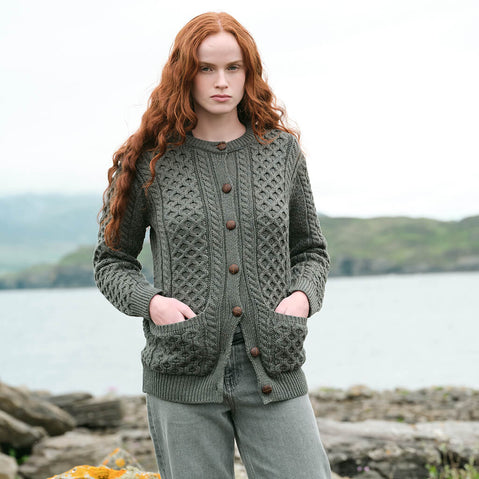 Image featuring The Banna Aran Cardigan in Tundra, crafted with authentic Irish Aran cable knit patterns, a timeless button-front silhouette, and practical front pockets, showcasing traditional Irish craftsmanship against a scenic coastal landscape.
