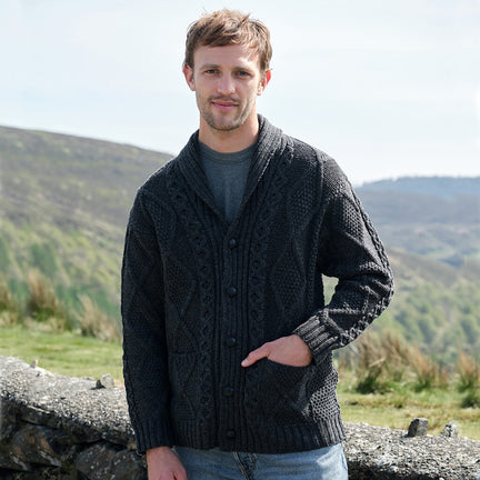 Man wearing a dark knitted cardigan standing outdoors with mountains in the background