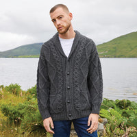 Man wearing a charcoal Men's Heritage Aran Shawl Collar Button Cardigan standing by a lake with mountains in the background