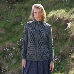 Women's Traditional Aran Zip Front Cardigan in Tundra Marl, featuring authentic Irish cable knit stitching, a full zip-front design, and practical pockets, styled in the Irish countryside surrounded by wildflowers and rolling green landscapes.