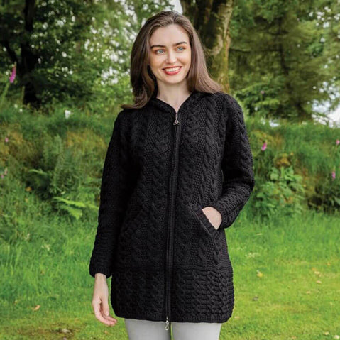 Woman wearing a black Aran zipper cardigan standing in a natural setting with greenery.