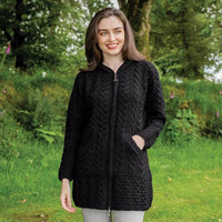 Woman wearing a black knitted jacket standing in a natural setting with greenery.